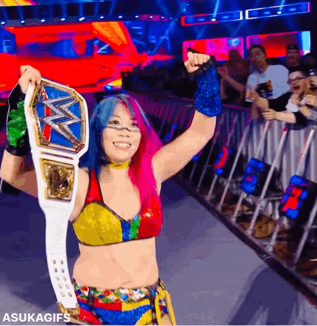 a female wrestler is holding a championship belt in front of a crowd and says asukagifs at the bottom