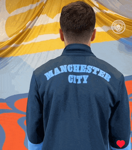a man wearing a manchester city shirt stands in front of a yellow and blue flag