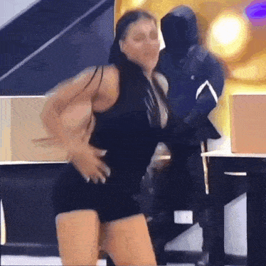 a woman in a black tank top and shorts is dancing in front of a man in a mask .
