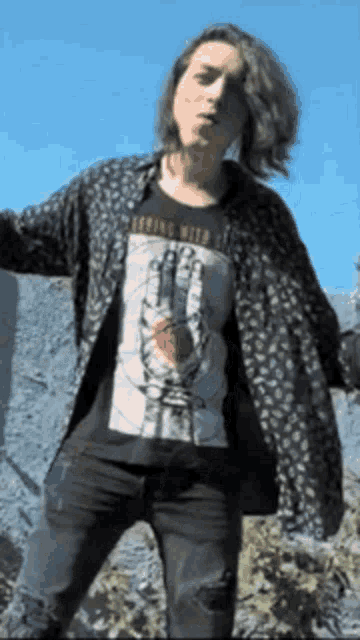 a woman wearing a t-shirt with a hand on it is standing in front of a rock wall .