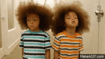 two young boys with big afros standing next to each other in a hallway .