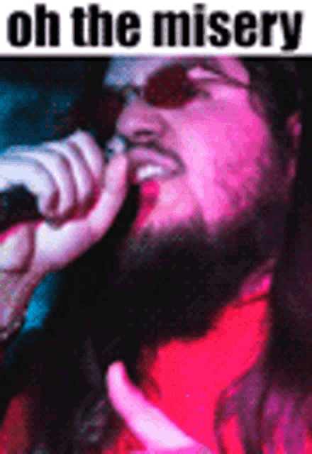 a man with a beard is singing into a microphone while wearing sunglasses and a red shirt .