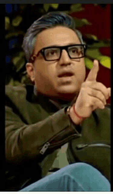 a man wearing glasses and a green jacket is pointing his finger