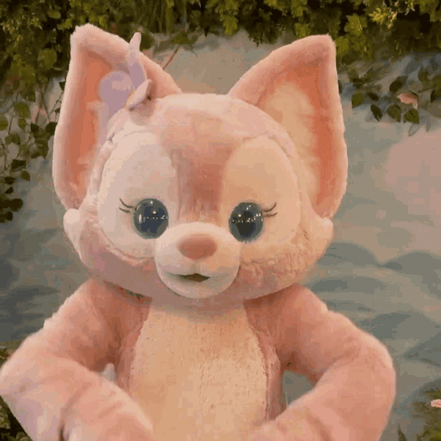 a pink stuffed animal with blue eyes and a bow on its ear