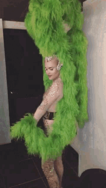 a woman in a green feathered costume is standing in a room