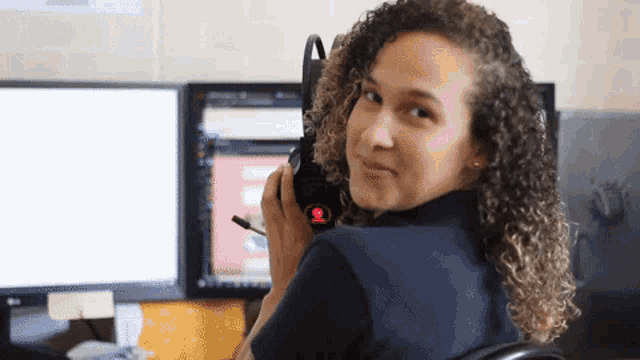 a woman sitting in front of a computer holding a microphone with a red button that says ' emergency ' on it