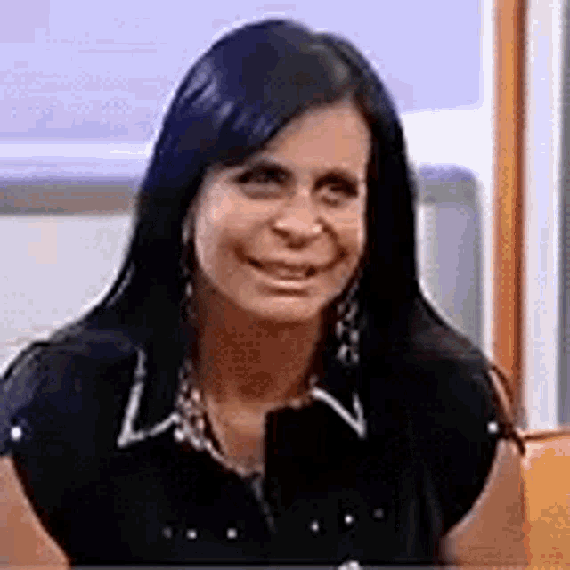a woman with long black hair is sitting on a couch and smiling .