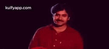 a man in a red shirt is waving his hand in front of his face .