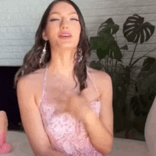 a woman in a pink dress is sitting on a couch with her eyes closed and her hands on her chest .