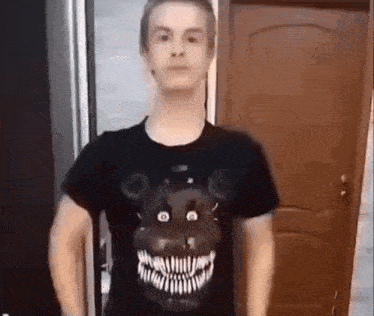 a man wearing a black t-shirt with a teddy bear on it is standing in front of a door .