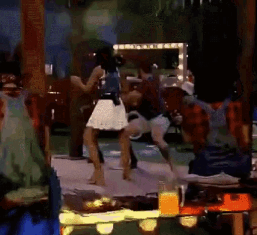 a group of people are dancing in a room with a bottle of orange juice on the table