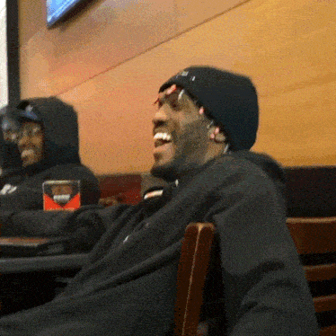 a man wearing a black hat with the letter i on it laughs