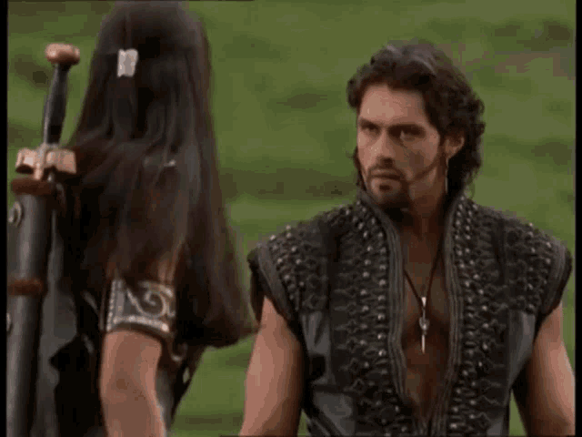 a man and a woman are standing next to each other in a field and the woman is holding a sword