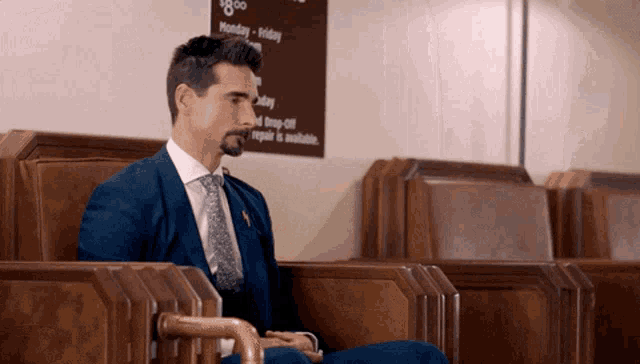 a man in a blue suit and tie sits in front of a sign that says monday - friday