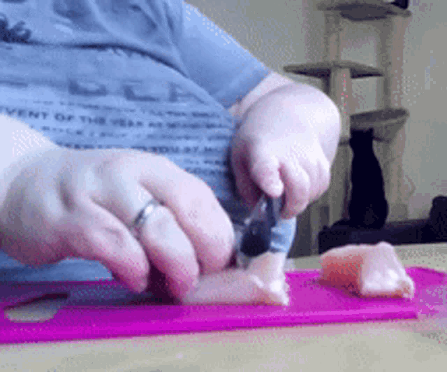 a person cutting a piece of meat on a cutting board with a cat in the background