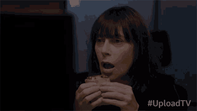 a woman is eating a sandwich in front of a tv screen with #uploadtv written below her