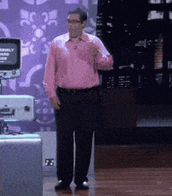 a man in a pink shirt and black pants stands in front of a screen that says terribly sad