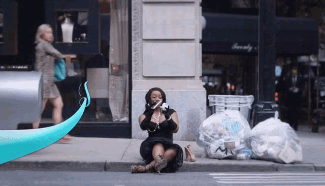 a woman sits on a sidewalk talking on a cell phone