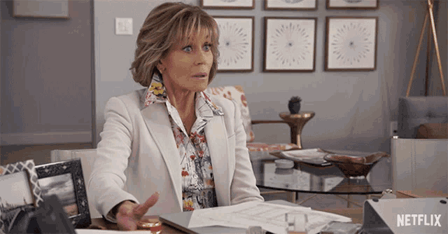 a woman sits at a desk with a netflix logo on the bottom right