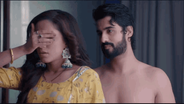 a shirtless man stands next to a woman who covers her eyes with her hand
