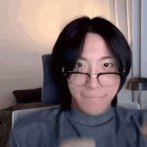 a man wearing glasses and a turtleneck is sitting in a chair and smiling .