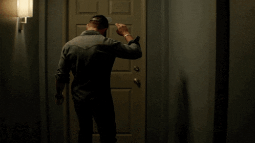 a man in a baseball cap is standing in front of a door with his hand on it