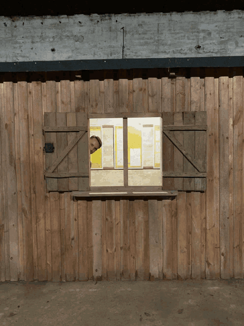 a man looks out of a wooden window with shutters