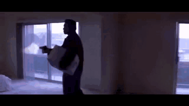 a silhouette of a man holding a pillow and a gun in an empty room .