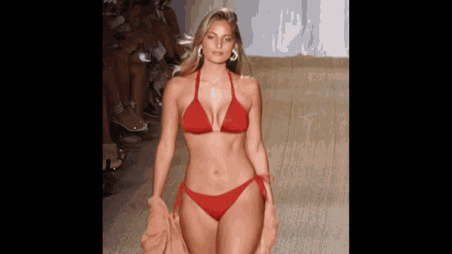 a woman in a red bikini walks down the runway at a fashion show