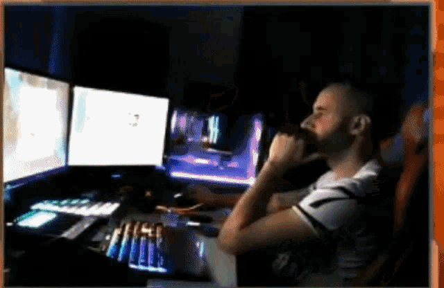 a man sits at a desk with three computer monitors and a keyboard ..