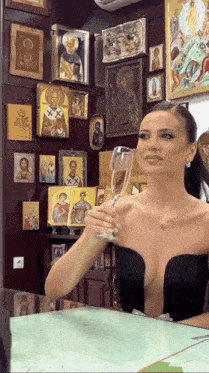 a woman is holding a glass of champagne in front of a wall of religious icons