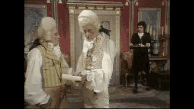 a man in a wig is holding a piece of paper in a room with other men .