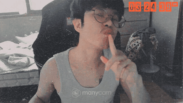 a man wearing glasses and a tank top is making a shhh gesture in front of a screen that says manycam