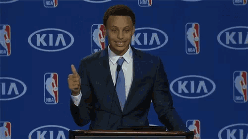 a man in a suit and tie giving a thumbs up in front of a kia background