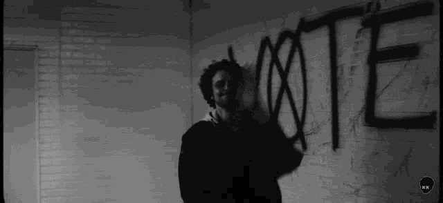 a black and white photo of a man standing in front of a wall with graffiti on it .