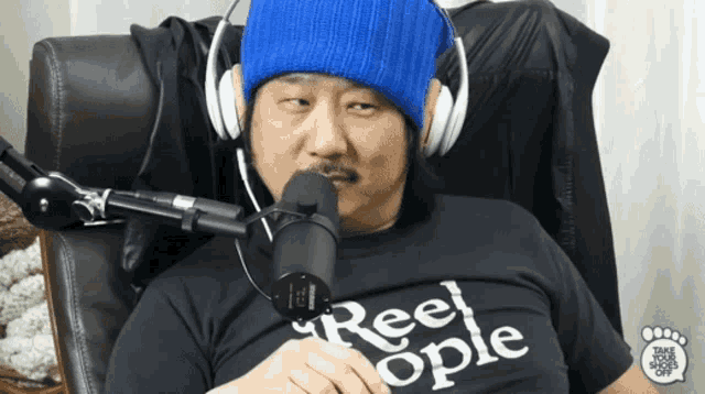 a man wearing headphones and a shirt that says reel ople is sitting in front of a microphone