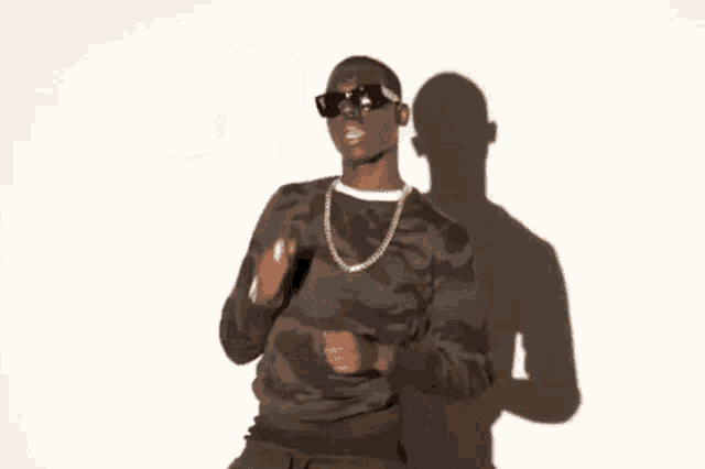 a man wearing sunglasses , a necklace , and a camouflage shirt is giving the middle finger .