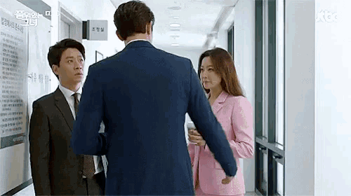 a man in a suit and a woman in a pink suit are standing in a hallway .