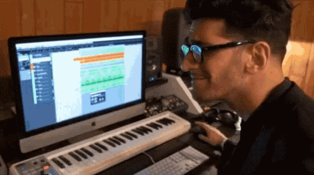 a man wearing glasses is playing a keyboard in front of a computer monitor