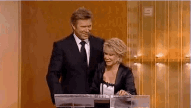 a man and a woman are standing next to each other at a podium . the man is wearing a suit and tie .