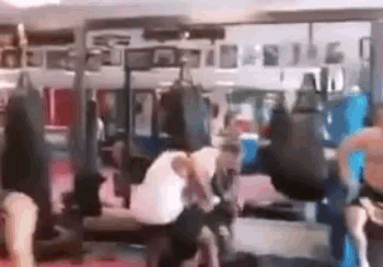 a group of people are fighting in a gym with punching bags hanging from the ceiling .