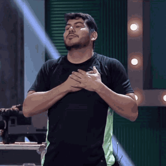a man with his hands on his chest is wearing a black shirt with green stripes