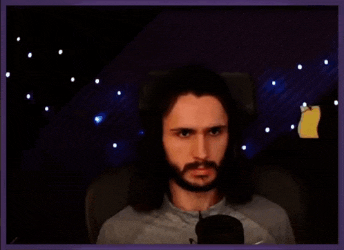 a man with long hair and a beard is sitting in front of a microphone and making a funny face