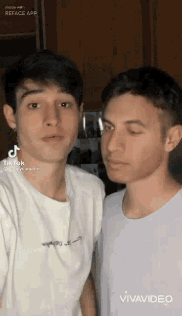 two young men are standing next to each other in a room and looking at the camera .