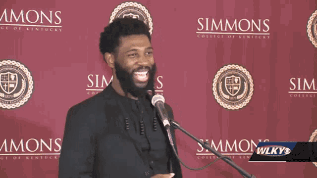 a man is speaking into a microphone in front of a simmons college of kentucky banner