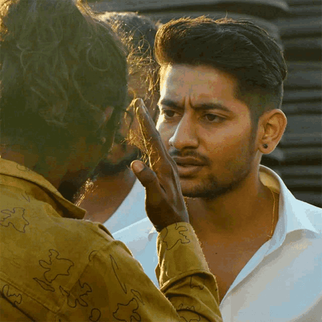 a man in a yellow shirt with the letter s on it touches the face of another man