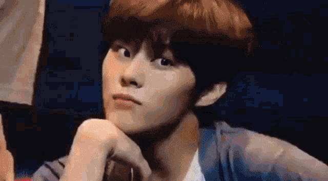a close up of a young man with his hand on his chin and looking at the camera .