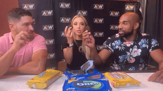 three people eating oreos in front of a wall that says aew on it