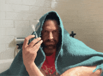 a man wrapped in a blue blanket holds a hourglass in front of his face