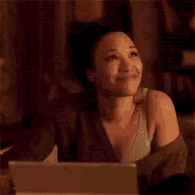 a woman is sitting at a table in front of a laptop computer and smiling .